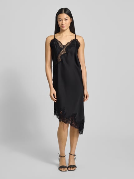 Frauenmodel trägt Kleid aus Satin mit Spitze Modell 'Sorelle' von Neo Noir, schwarzer Satin-Look, Asymmetrischer-Look, Minikleid mit Spaghettiträgern, Ganzkörperansicht von vorne.