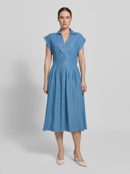 Frauenmodel trägt mittelblaues Hemdkleid aus Denim, weich fallender Stoff, Knopfleiste, A-Linie, Ganzkörperansicht von vorne.