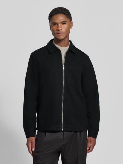Männermodel trägt Jacke mit Brusttasche und Kentkragen Modell 'ROLFSTED' von Casual Friday in Schwarz, gerader Schnitt, Ganzkörperansicht von vorne.