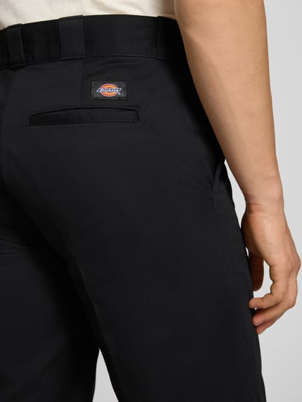 Männermodel trägt Bermudas mit französischen Eingrifftaschen von Dickies aus schwarzer, reiner Baumwolle, Straight Fit, Nahaufnahme Rückansicht.