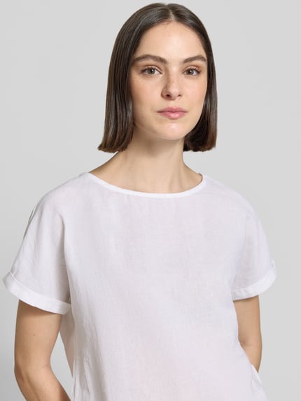 Modelka nosi bluzka lniana 'Leinenbluse mit fixiertem Ärmelaufschlag' od Christian Berg Woman, czysty len, krój straight fit, okrągły dekolt, rękawy z zakładką, długość tyłu w rozmiarze 36: 60 cm, długość rękawów w rozmiarze 36: 10 cm, gładka biała tkanina, proste kształty, miękka tekstura, zbliżenie na górną część ciała.