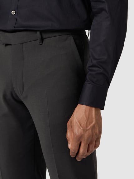 Männermodel trägt Stoffhose mit Bundfalten von Drykorn in Dunkelgrau, Material-Mix mit Baumwoll-Anteil, Nahaufnahme Oberkörper.