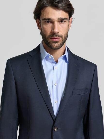 Männermodel trägt 2-Knopf-Sakko mit Reverskragen Modell 'Sono' von windsor., dunkelblau, glatte Textur, Nahaufnahme Oberkörper, Schurwolle-Elasthan-Mix, unifarben, Brusttasche sichtbar.