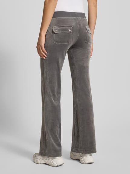 Frauenmodel trägt Low Rise Sweatpants mit elastischem Bund Modell 'LAYLA' von Juicy Couture aus grauem, weichem Baumwoll-Mix mit Stretch-Anteil, Flared-Cut, aufgesetzte Eingrifftaschen, samtiger Textur, Ganzkörperansicht Rückansicht.