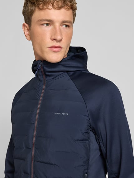 Männermodel trägt Hybrid Jacke mit Kapuze Modell 'PERFECT' von JACK & JONES, navy, Logo-Print, Nahaufnahme Oberkörper. Kontext: Herren Hybrid Jacke, gerader Schnitt, Kapuze, Reißverschluss, seitliche Reißverschlusstaschen, Rückenlänge 67 cm, Schulterbreite 44 cm, Brustweite 51 cm, Ärmellänge 69 cm.