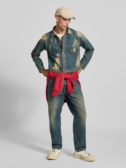 Męski model nosi Regular Fit Jeansjacke aus Baumwolle od KENZO w Efekt znoszenia, niebieski odcień, nakładana brustasza, listwa guzikowa na całej długości, Długość tyłu w rozmiarze M: 58 cm, Szerokość w rozmiarze M: 48 cm, Długość rękawów w rozmiarze M: 63 cm, widok całej sylwetki z przodu.