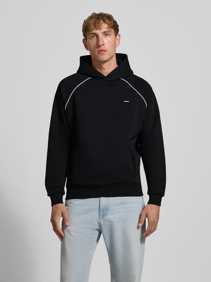 Männermodel trägt Hoodie mit Logoprint und Kontrastspipings von REVIEW, schwarze Farbe, Regular Fit, Baumwoll-Mix, Ganzkörperansicht von vorne.