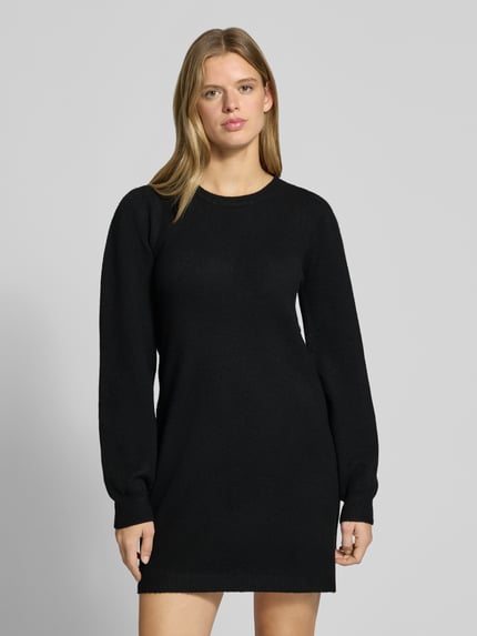 Frauenmodel trägt schwarzes Strickkleid mit Label-Detail von PIECES, glatte Struktur, Damen Freizeitkleid, Ganzkörperansicht von vorne.