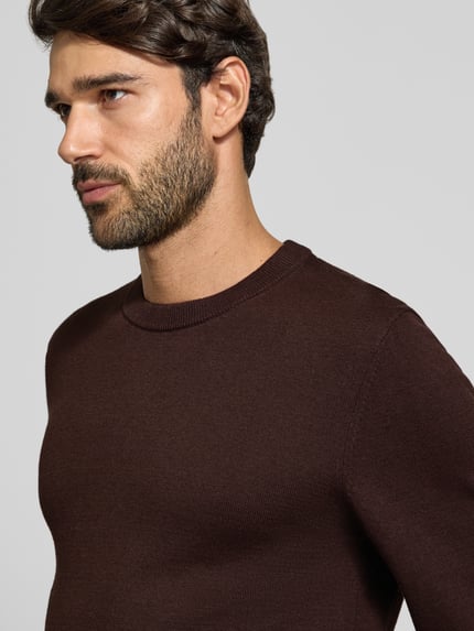 Männermodel trägt Strickpullover aus Baumwoll-Kaschmir-Mix mit Rundhalsausschnitt von MCNEAL, dunkelbraun, feine Textur, Nahaufnahme Oberkörper, Regular Fit, Rückenlänge 70 cm, Ärmellänge 74 cm.