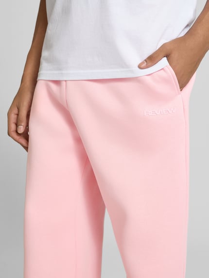 Männermodel trägt Straight Fit Sweatpants Baumwoll-Mix von REVIEW in Rosa, Label-Print, seitliche Eingrifftaschen, Nahaufnahme Oberschenkel.