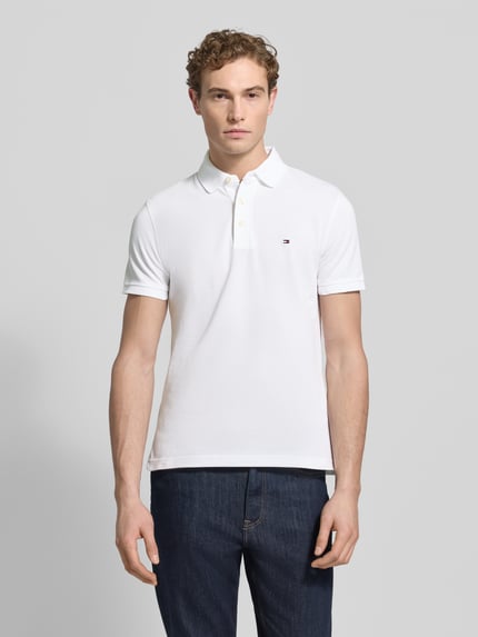 Männermodel trägt Slim Fit Poloshirt mit Stretch-Anteil von Tommy Hilfiger aus Baumwoll-Elasthan-Mix, Polokragen, Logo-Stickerei, Ganzkörperansicht von vorne.