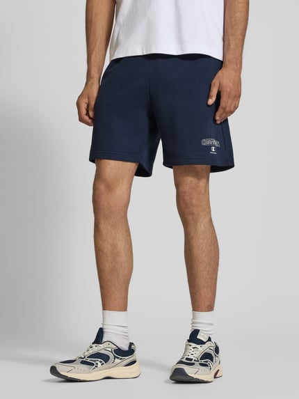 Männermodel trägt dunkelblaue Sweatshorts mit Logo und elastischem Bund von CHAMPION aus Baumwoll-Mix, Regular-Fit, Nahaufnahme Oberschenkel.