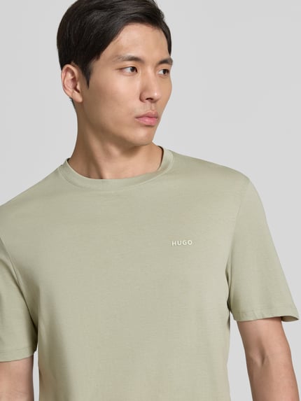 Męski model nosi Regular Fit T-Shirt aus reiner Baumwolle Modell 'DERO222' von HUGO, efekt: jednolity kolor, krój regular fit, nadruk z logo, okrągły dekolt, krótki rękaw, dżersej, bawełna; zbliżenie górnej części ciała.