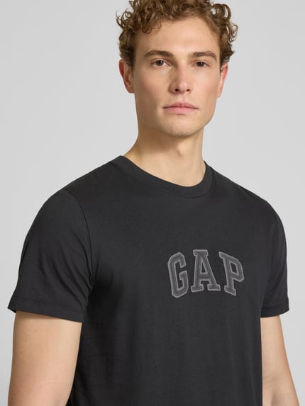 Männermodel trägt T-Shirt mit Logo-Patch und Rundhalsausschnitt von GAP in Schwarz, reine Baumwolle, Straight Fit, Nahaufnahme Oberkörper.