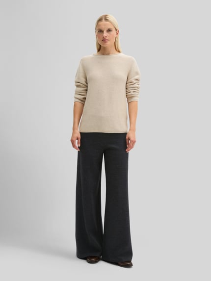 Modelka kobieca ma na sobie Regular Fit Pullover aus reiner Baumwolle von MARC O'POLO w jednolitym, beżowym kolorze i dzianinowej fakturze, z długimi rękawami, dekoltem typu łódka, bocznymi kieszeniami i ściągaczem tunelowym, materiał czysta bawełna, widok całej sylwetki z przodu.