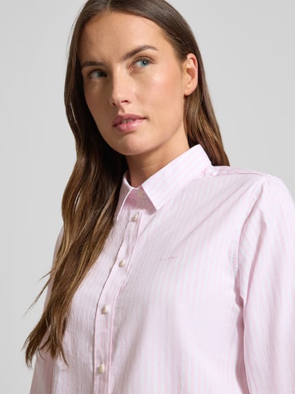 Vrouwenmodel draagt Hemdbluse uit katoen met streepmotief van GANT, recht model, overhemdkraag, labeldetail, knoopsluiting, met lange mouwen. Nahaufnahme bovenlichaam.