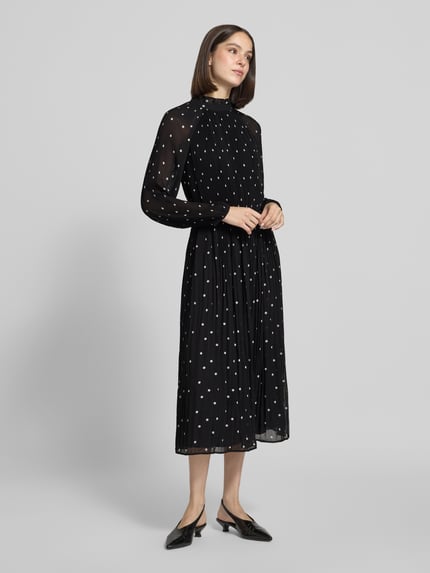 Frauenmodel trägt Midikleid im Allover-Look mit Plisseefalten von COMMA, schwarz mit weißen Punkten, Ganzkörperansicht von vorne.