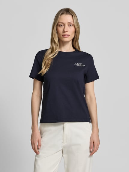 Frauenmodel trägt T-Shirt mit Label-Print und Rundhalsausschnitt von Gant, damski t-shirt z bawełny, krój regular fit, nadruk z logo, okrągły dekolt, długość tyłu w rozmiarze S: 57 cm, kolor granatowy, prosta faktura, Ganzkörperansicht von vorne.