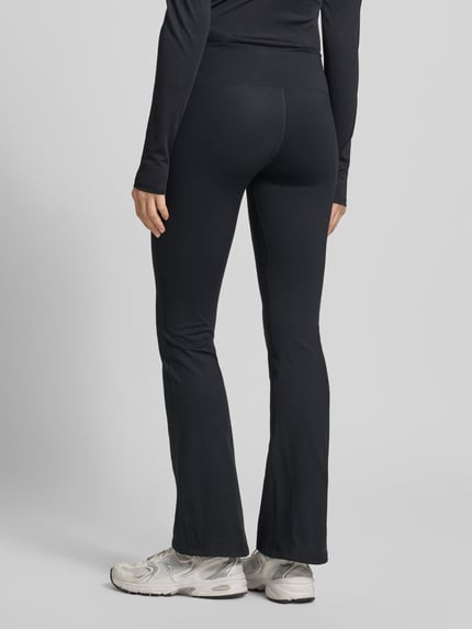Frauenmodel trägt Flared Cut Leggings mit Logo von NIKE TRAINING, schwarz, elastischer Bund, Material-Mix, Ganzkörperansicht Rückansicht.