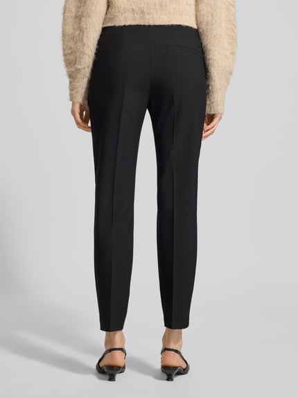 Vrouwenmodel draagt Regular Fit Schmale Hose mit Bügelfalten von s.Oliver BLACK LABEL, look: effen, persplooien, tailleband met structuur, elastische boord, steekzakken, aangeduide achterzakken, labelstitching applicatie, mid waist pasvorm; volledig lichaam zicht achterkant.