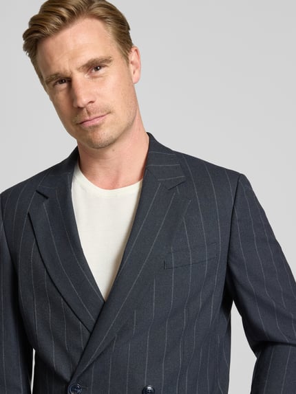 Männermodel trägt Sakko mit seitlichen Eingrifftaschen und Reverskragen von MCNEAL in Dunkelblau mit Nadelstreifen, Nahaufnahme Oberkörper. Regular Fit, Zweireiher, Brustleistentasche, feine Textur.
