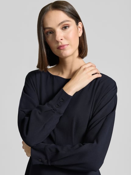 Frauenmodel trägt Midikleid mit Rundhalsausschnitt von Christian Berg Woman Selection in dunklem Blau, fließender Stoff, glatte Textur, lange Ärmel, Kontext: A-Linie, Teilungsnaht, rückseitiger Reißverschluss, Rückenlänge 110 cm, Brustweite 39 cm, Ärmellänge 62 cm, Nahaufnahme Oberkörper.