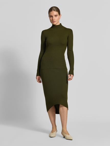 Frauenmodel trägt Longsleeve aus Woll-Mix von Victoria Beckham in Olivgrün, eng anliegende Ripp-Strick-Optik, Stehkragen, Ganzkörperansicht von vorne.