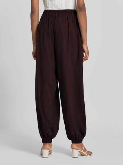 Frauenmodel trägt Balloon Fit Stoffhose aus Viskose-Mix Modell 'Hamy' von FREE/QUENT in Dunkelbraun mit elastischem Bund und Beinabschlüssen, Ganzkörperansicht Rückansicht.