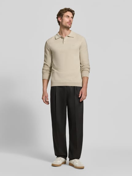 Męski model nosi beżową koszulkę polo Relaxed Fit Poloshirt mit Woll-Anteil Modell 'KN_Momentum-X PL' od BOSS Green, czarne spodnie, białe buty, jasnoszare, gładkie tło, pełny widok z przodu.