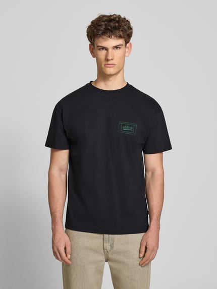Männermodel trägt Regular Fit T-Shirt mit Logo-Print von BLKVIS aus Reine Baumwolle, dunkle Farbe, Rundhalsausschnitt, Ganzkörperansicht von vorne. Rückenlänge bei Größe M: 67 cm.