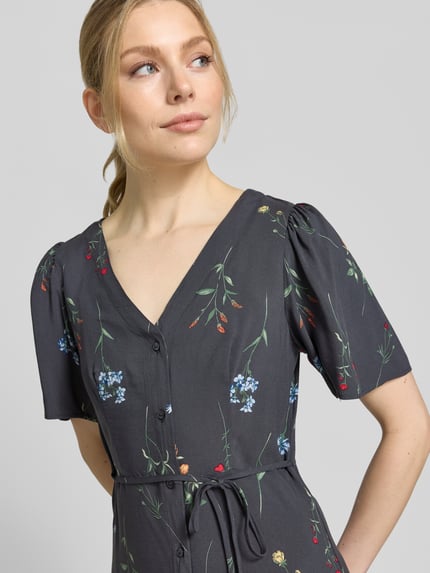 Vrouwenmodel draagt Leicht ausgestelltes Minikleid aus reiner Viskose Modell 'ALBA' van Vero Moda, uni-look, licht uitlopend, mini, V-hals, korte wijde mouwen, bindriem, knopen, puur viscose, close-up bovenlichaam.