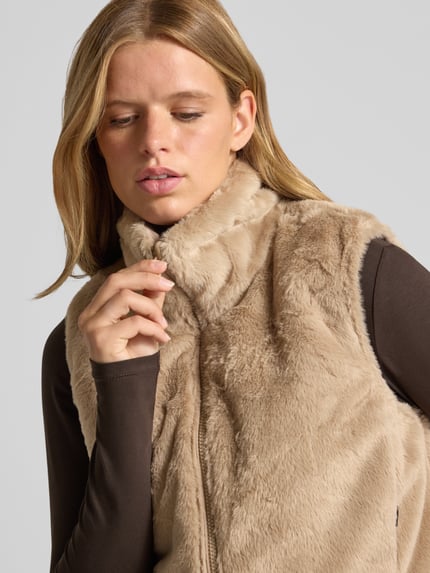 Vrouwenmodel draagt Regular fit bodywarmer met wendefunctie model 'DANA' van ONLY in beige met zachte textuur, Nahaufnahme bovenlichaam. Context: Dames bodywarmer van ONLY.