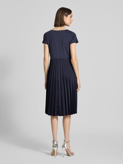 Modelka nosi Midikleid in Plissee-Optik od Christian Berg Woman Selection, granatowy kolor, elastyczny materiał, krój slim fit, plisowana faktura, okrągły dekolt, krótkie rękawy, długość tyłu w rozmiarze 36: 108 cm, szerokość w rozmiarze 36: 42 cm, długość rękawa w rozmiarze 36: 15 cm, widok całej sylwetki z tyłu.