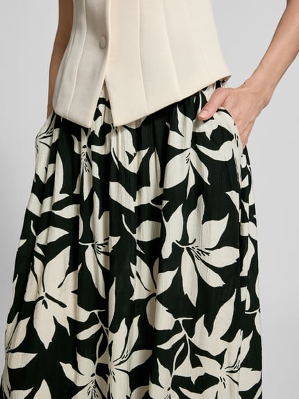 Vrouwenmodel draagt Relaxed Fit Uitlopend Midi-Rok uit viscosemix van s.Oliver RED LABEL met all-over bloemenmotief, popeline, elastische boord, midilengte, detailopname taille en heupen.