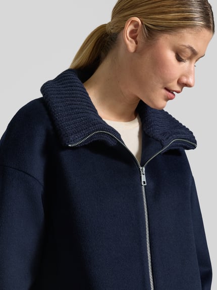 Frauenmodel trägt Mantel aus Woll-Mix mit Reißverschlusstaschen von White Label, dunkelblau, sichtbarer Stehkragen, Nahaufnahme Oberkörper.