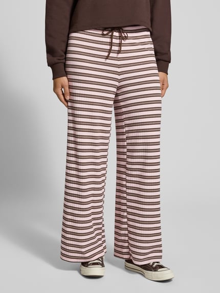 Frauenmodel trägt Lounge-Hose mit Streifenmuster von Gina Tricot in Rosa und Braun, elastischer Bund, Relaxed Fit, Ganzkörperansicht von vorne.