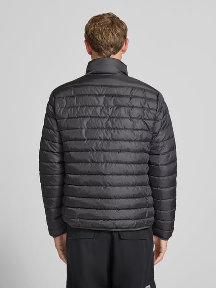 Männermodel trägt dunkelgraue, gesteppt strukturierte Jacke mit Label-Patch Modell 'ELVIS' von JACK & JONES, Ganzkörperansicht Rückansicht. Gerader Schnitt, Stehkragen, Reißverschluss, seitliche Reißverschlusstaschen, Maße laut Kontext.