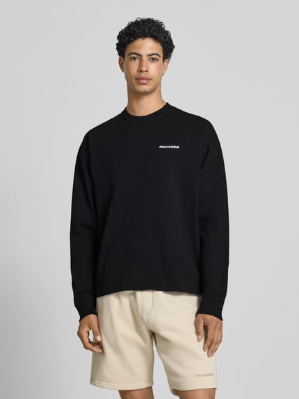 Männermodel trägt Oversized Sweatshirt mit Logo-Stitching Modell 'Rusk' von Pegador in Schwarz aus Reine Baumwolle, Oversized-Fit, Ganzkörperansicht von vorne. Rückenlänge bei Größe M: 61 cm.