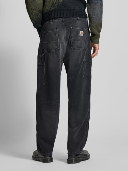 Männermodel trägt Wide Fit Jeans Logo-Patch Modell 'Grind' von Carhartt Work In Progress in Schwarz mit 5-Pocket-Design aus reiner Baumwolle, Ganzkörperansicht Rückansicht.