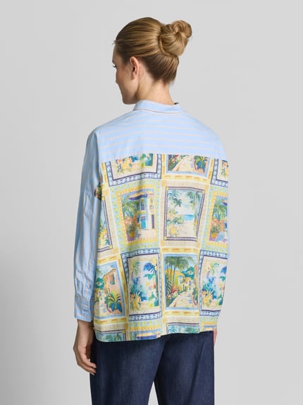 Vrouwenmodel draagt Relaxed Fit damesblouse met strepenpatroon van Emily Van den Bergh, puur katoen, overhemdkraag, knoopsluiting, lengte rug 65 cm, mouwlengte 41 cm, meerkleurig met lichte en blauwe strepen, achterzijde met kleurrijke prints, voorkant geheel zichtbaar, kleur- en textuurcontrast, volledige achteraanzicht