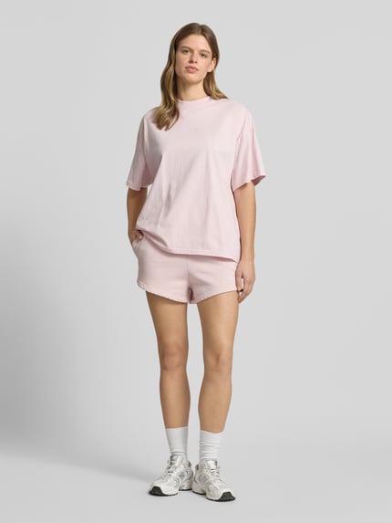 Frauenmodel trägt High Waist Shorts mit Logo-Stitching Modell 'WILUNA' von Pegador in Rosa, Baumwoll-Mix, französische Eingrifftaschen, elastischer Bund, Bundweite 40 cm, Innenbeinlänge 7 cm, Ganzkörperansicht von vorne.