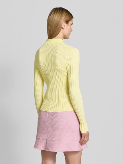 Frauenmodel trägt Strickjacke aus Viskose-Mix mit Umlegekragen von Marc Cain in Gelb, Slim-Fit, Ripp-Optik, Knopfleiste, Ganzkörperansicht Rückansicht, Rückenlänge 54 cm und Ärmellänge 65 cm bei Größe 36, dazu rosa Rock.