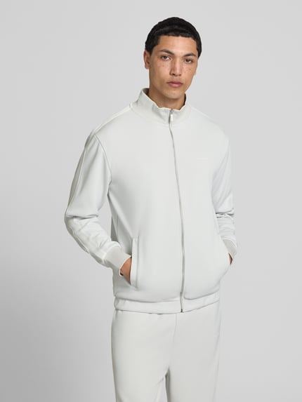 Männermodel trägt Jacke mit Stehkragen und Eingrifftaschen Modell 'Viro' von Pegador, heller Material-Mix, Regular-Fit, Reißverschluss, Ganzkörperansicht von vorne. Rückenlänge bei Größe M: 70 cm, Ärmellänge bei Größe M: 65 cm.