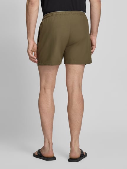 Männermodel trägt Relaxed Fit Badeshorts mit Logo-Stitching von Emporio Armani in Oliv, Elastischer Bund mit Tunnelzug, Ganzkörperansicht Rückansicht.