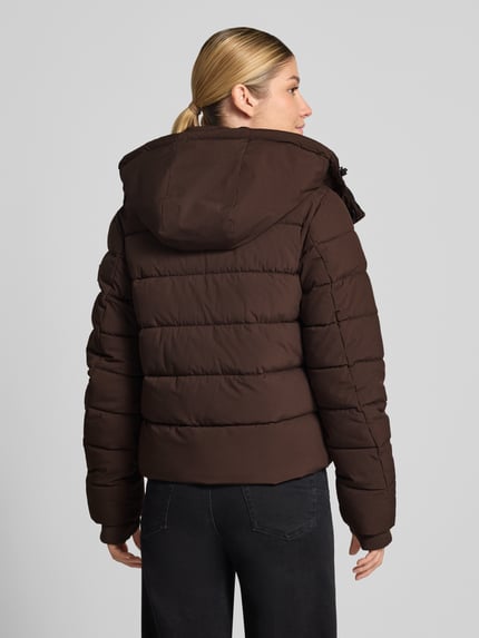 Frauenmodel trägt Jacke mit Daumenloch und Kapuze von NAUTGÅRD in Dunkelbraun, gerader Schnitt, Steppstruktur, detailreiche Texturen, Ganzkörperansicht Rückansicht. Rückenlänge 58 cm, Schulterbreite 40 cm, Brustweite 48 cm, Ärmellänge 65 cm.