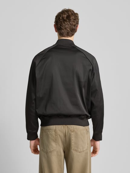Mężczyzna nosi Bomberjacke mit Reißverschluss od ARMANI EXCHANGE, czarny materiał, regular fit, ściągacze, widok całej sylwetki od tyłu.