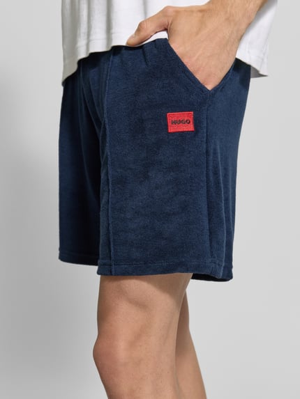 Männermodel trägt Regular Fit Sweatshorts aus Baumwoll-Mix Modell 'TERRANCE' von HUGO, Optik: Unifarben, Label-Patch, Nahaufnahme Oberschenkel.
