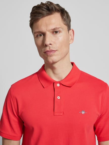 Männermodel trägt Slim Fit Poloshirt mit Logo-Stitching von Gant in Rot, reine Baumwolle, Polo-Kragen, Nahaufnahme Oberkörper.
