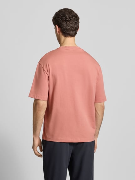 Männermodel trägt Relaxed Fit T-Shirt aus reiner Baumwolle Modell 'RELEXASPEN' von SELECTED HOMME in unifarbenem Rosa, Feinrippstruktur, Ganzkörperansicht Rückansicht.