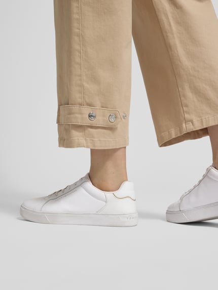 Frauenmodel trägt Wide Fit Hose mit Eingrifftaschen von Marc Cain aus elastischem Baumwoll-Mix in Beige, Detailaufnahme Beinabschluss.